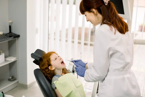 Piękny uśmiech z białymi zębami. Dentysta bada jamę ustną młodej pięknej dziewczyny przez lupę w gabinecie stomatologicznym.. — Zdjęcie stockowe