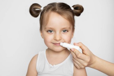 Dudaklar hijyen ve bakım. Güneş kremi, rüzgar ve çocuk dudakları için don koruması. Annenin elinin yatay çekimini kapat, mutlu gülümseyen güzel kızın dudaklarına dudak merhemi sür.