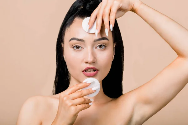 Κοντινό πλάνο οριζόντια στούντιο της όμορφης νεαρής όμορφης γυμνής ασιάτισσας γυναίκας με υγιές φρέσκο δέρμα, που ποζάρει απομονωμένη πάνω από μπεζ φόντο, κρατώντας βαμβακερά μαξιλαράκια. Καθαρισμός και περιποίηση δέρματος — Φωτογραφία Αρχείου