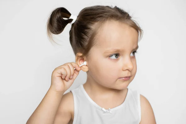 Ear cleaning, skincare concept. Little attractive kid girl, looking aside, cleaning her ear with cotton swab, posing on isolated white background. Childs hygiene concept — Stock Photo, Image