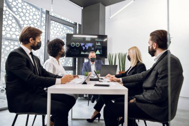 Covid-19 salgını açısından iş kavramı. Yüz maskeli çok ırklı iş adamları, ofis odasında toplantı, şirket stratejisi ve proje tartışmaları.