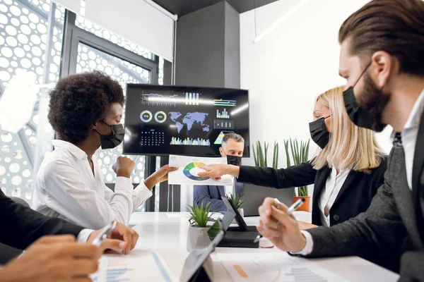 Équipe d'hommes et de femmes d'affaires multiraciaux axés sur les professionnels, effectuant un remue-méninges et discutant d'infographie tout en étant assis à la table dans une salle de réunion moderne à l'intérieur — Photo