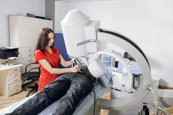 Extracorporeal Shock Wave Lithotripsy. Young female doctor in red uniform performing lithotripsy procedure for male patient, using modern equipment, ultrasonic lithotripter to break up kidney stones — Stock Photo, Image