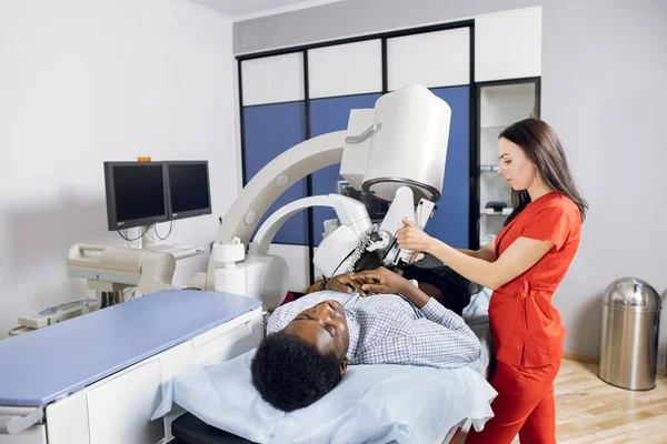 Treatment of urethral stones by non-invasive Extracorporeal Shock Wave Lithotripsy. Woman doctor providing the kidney stones lithotripsy for her male African patient in modern clinic — Stock Photo, Image