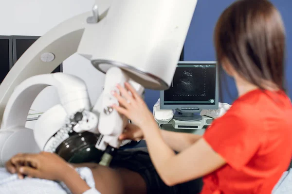 Extracorporeal Shock Wave Therapy. Kidney stone treatment. Back view of woman doctor looking at the digital screen of the lithotriptor to determine kidney stones position. Focus on ultrasound monitor — Stock Photo, Image