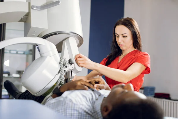 Procedure of extracorporeal shock wave lithotripsy in modern urology medical center. Close up of pretty Caucasian woman doctor providing stone treatment for black male patient using lithotripter — Stock Photo, Image