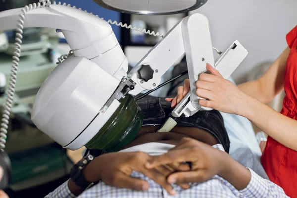 Close up cropped image of lying African man patient having procedure of lithotripsy. Hands of female doctor working with modern ultrasonic lithotripter to crush kidney or ureter stones — Stock Photo, Image