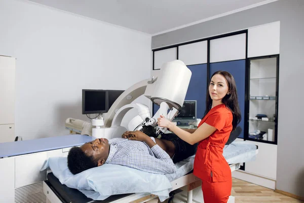 Treatment of urethral stones by non-invasive extracorporeal shock wave lithotripsy. Female professional doctor working with modern lithotripter to break up stones for her male patient — Stock Photo, Image