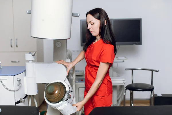 Portait of pretty confident focused Caucasian female doctor, wearing red medical uniform, working in modern clinic with ultrasonic lithotripter machine. Kidney stones treatment concept — Stock Photo, Image