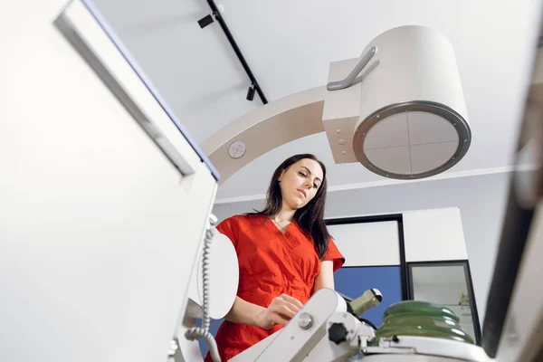 Bottom view of young attractive Caucasian female doctor in red uniform, working with modern lithotripter equipment for treatment of kidney stones. Non-invasive extracorporeal shock wave lithotripsy — Stock Photo, Image