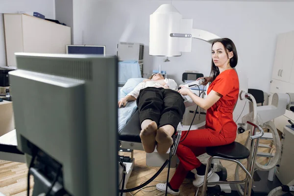 Terapia de ondas de choque extracorpóreas. Tratamento de pedra nos rins. Visão frontal da mulher médica olhando para a tela digital do litotriptor para determinar a posição de pedras da paciente mulher — Fotografia de Stock