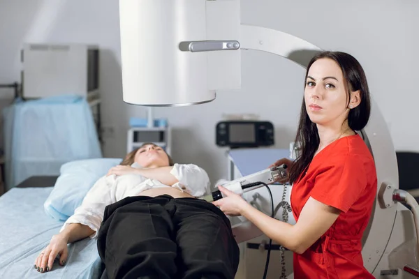 Treatment of urethral stones by non-invasive extracorporeal shock wave lithotripsy. Woman doctor working with modern lithotripter to crush kidney stones for her female patient in modern clinic — Stock Photo, Image