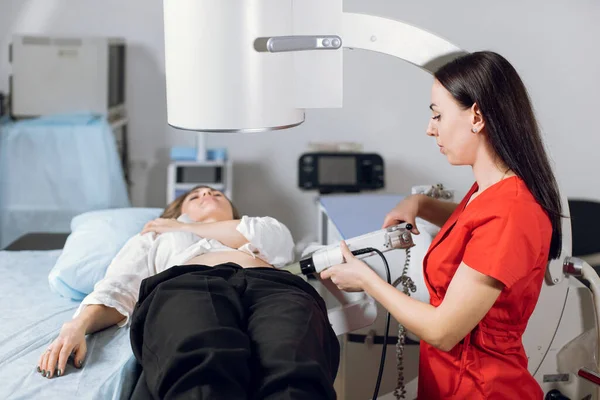 Treatment of urethral stones by non-invasive extracorporeal shock wave lithotripsy. Professional woman doctor working with modern lithotripter to break up stones for her female patient — Stock Photo, Image