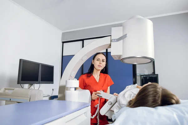 Porträt einer jungen attraktiven Ärztin, die in die Kamera blickt, während sie Lithotripsie-Verfahren und Ultraschalluntersuchungen für ihre kaukasische Patientin mit modernem Ultraschall-Lithotriptor durchführt — Stockfoto