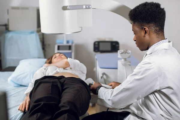 Treatment of urethral stones by non-invasive extracorporeal shock wave lithotripsy. Professional black man doctor working with modern lithotripter to break up stones for his female patient — Stock Photo, Image