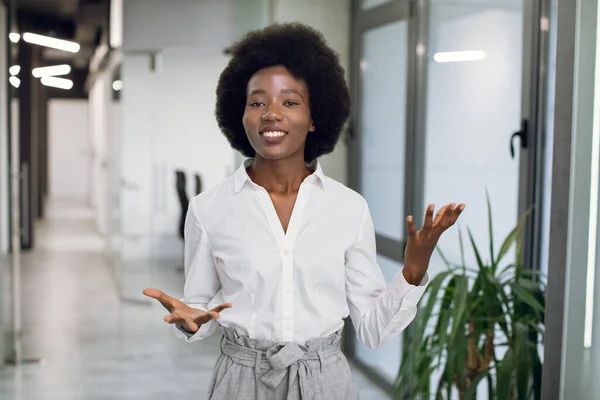 Jonge aantrekkelijke en succesvolle zwarte afro-Amerikaanse zakenvrouw in formele kleding, het geven van een interview, spreken en gebaren, terwijl binnen in een modern kantoorgebouw — Stockfoto