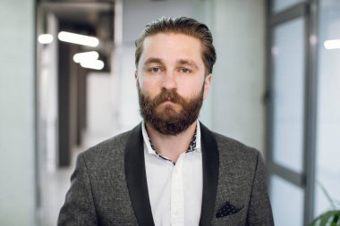 İş adamı, patron ya da CEO, takım elbiseli, kameraya bakan, modern ışık ofisinin arka planında duran yakışıklı iş adamının yüz portresini kapat.