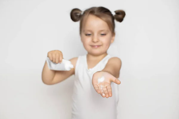 Alegre linda niña sosteniendo tubo con crema protectora, y mostrando su pequeña mano con crema a la cámara. Primer plano retrato sobre fondo blanco aislado. Concéntrate en la mano — Foto de Stock