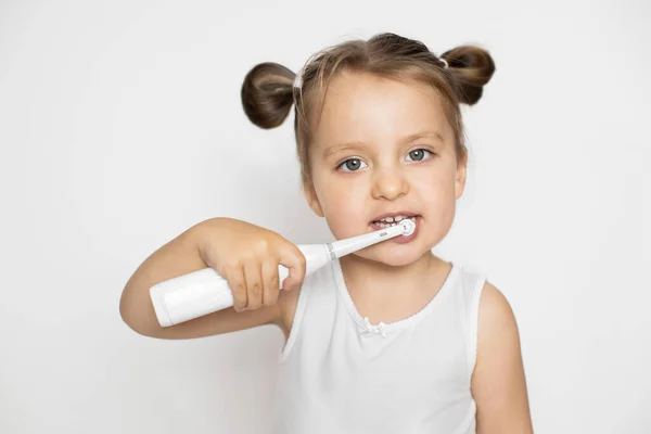 Pequeña chica rubia linda cepillándose los dientes con un cepillo de dientes eléctrico. Cuidado dental oral y prevención de caries. Primer plano horizontal plano de estudio sobre fondo blanco aislado — Foto de Stock