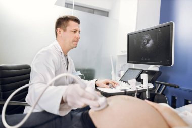 Modern hastanede hamile bir kadın için ultrason taraması yapan profesyonel odaklı beyaz erkek doktorun yan görüntüsü. Doktorun yüzüne odaklan.
