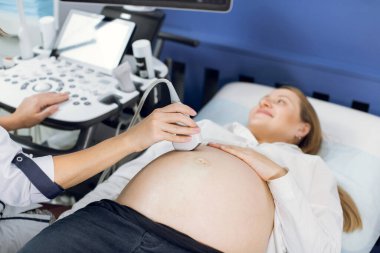 Doktorların ellerini kapat, modern ultrason cihazlarını kullanarak hamile bir kadının karnını tara ve özel bilgisayar tuşlarına bas.