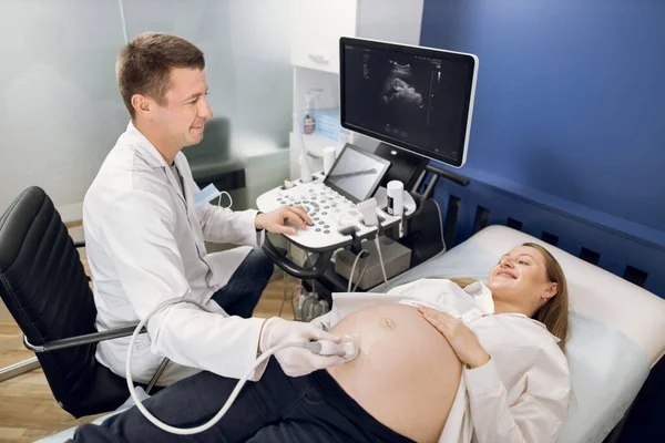 Médico obstetra sorridente, examinando a barriga da mulher grávida feliz por ultra-som. Médico alegre fazendo procedimento de ultrassom para seu paciente, olhando um para o outro. Visão de ângulo superior — Fotografia de Stock