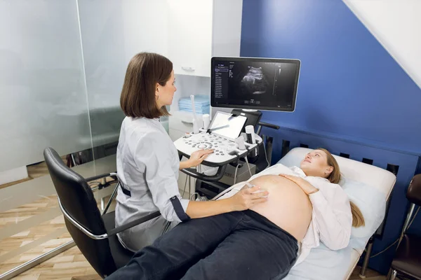 Mulher grávida recebendo ultra-som ultra-sonografia, enquanto jovem obstetrista médico concentrada explica o procedimento para ela — Fotografia de Stock