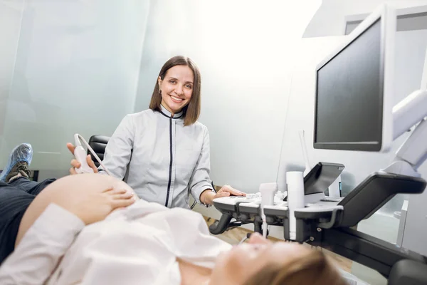 High-skilled professional attractive woman doctor doing 3d ultrasound on belly of pregnant woman in clinic, smiling to camera. Ultrasound for pregnant woman — Stock Photo, Image