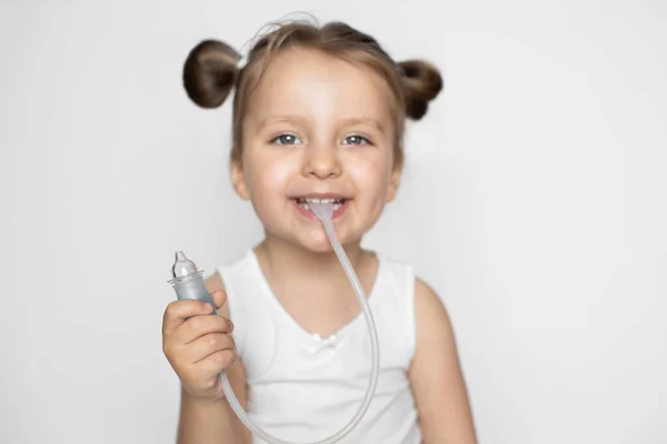 O conceito de medicina e higiene da criança. Aspirador nasal infantil. Bonito pequena menina sorridente com rabo de cavalo estilo de cabelo, mostrando a câmera aspirador nasal. Foco no aspirador — Fotografia de Stock