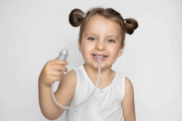 O conceito de medicina e higiene da criança. Aspirador nasal infantil. Bonito pequena menina sorridente com rabo de cavalo estilo de cabelo, mostrando a câmera aspirador nasal. Foco no rosto — Fotografia de Stock