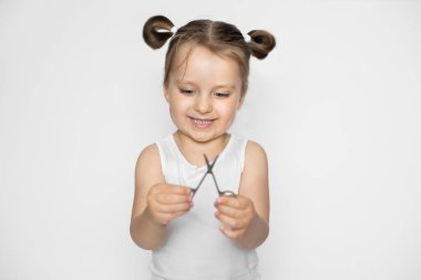 Dikkatli tırnak bakımı, çocukların hijyen konsepti. Sarı saçlı, elinde manikür makası tutan mutlu küçük kız banyodan sonra manikür ve bakım prosedürlerine hazır. Beyaz arkaplanda izole