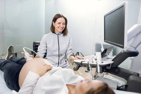 Medicina, cuidados de saúde e ultra-som conceito. Gravidez e obstetrícia. Feliz mulher satisfeita médico, fornecendo ultra-som de triagem para jovem grávida paciente — Fotografia de Stock