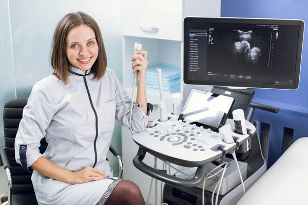 Alto qualificado profissional atraente mulher médico sonógrafo usando máquina de ultra-som no trabalho, sorrindo e olhando para a câmera — Fotografia de Stock