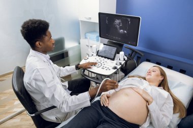 Ultrason testi. Hamilelik. Genç, Afrikalı erkek, jinekolog jinekoloğun hamile kadın hastasına ultrason taraması yapması.