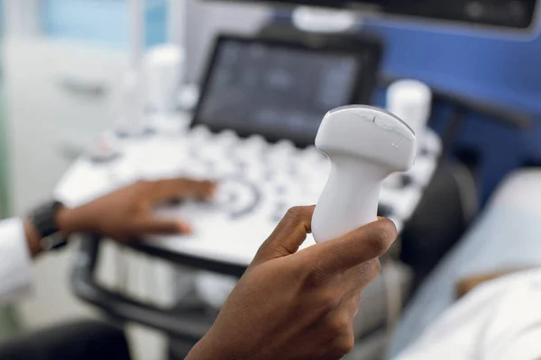 Закройте фотографию ультразвукового сканера в руках афроамериканского врача-мужчины. Диагностика. Сонография. Современная ультразвуковая машина на размытом фоне — стоковое фото