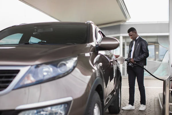 Açık hava benzin istasyonundaki genç Afrikalı Amerikalı adamın portresi. Lüks arabasına benzin dolduruyor, yakıt deposuna benzin tıkıştırıyor. — Stok fotoğraf
