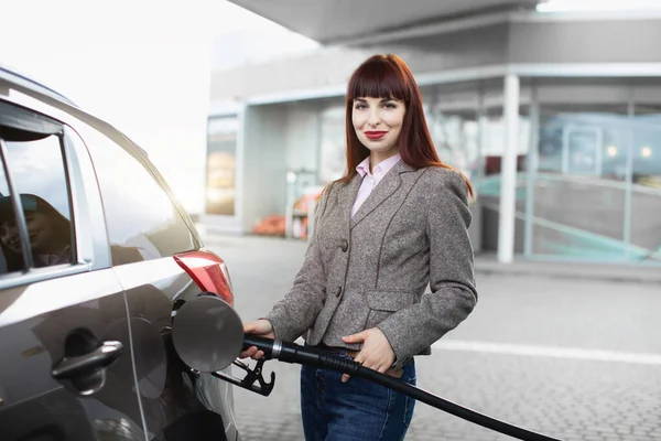 Güzel, beyaz saçlı, kot pantolon ve ceket giyen, lüks arabasını benzin istasyonunda benzinle dolduran bir kadın. — Stok fotoğraf
