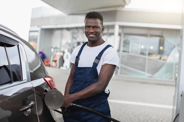 Çalışan, gülümseyen Afrikalı Amerikalı bir benzin istasyonu çalışanının portresi. İstasyonda benzin dolduran lüks bir araba. Benzin istasyonunda yakıt ikmali. — Stok fotoğraf