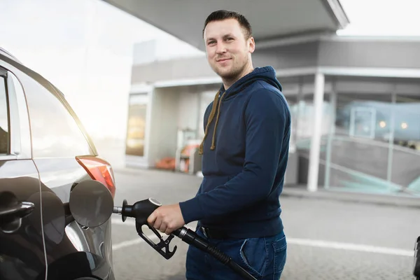 Primer plano retrato de joven guapo hombre caucásico, con ropa casual elegante, repostando su coche de lujo en la gasolinera al aire libre. Reabastecimiento del concepto de automóvil — Foto de Stock