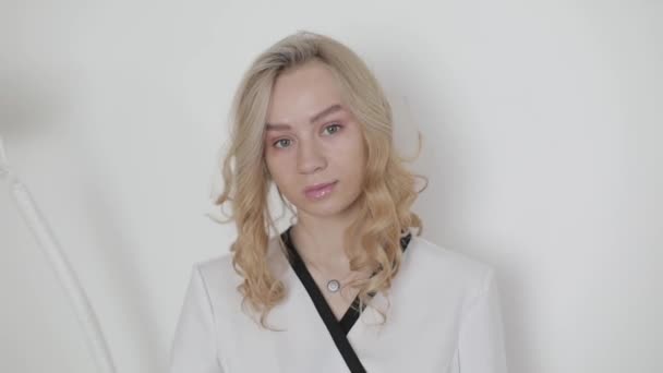 Pół długości portret młodej, ładnej blondynki białej kobiety kosmetolog lekarz demonstrujący strzykawkę w dłoniach na białym beżowym tle ściany w klinice kosmetycznej — Wideo stockowe