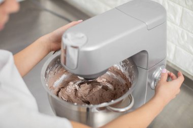 Önlükle yemek pişiren kadın mikser ya da hamur yoğurmak için yiyecek işlemcisi kullanıyor.