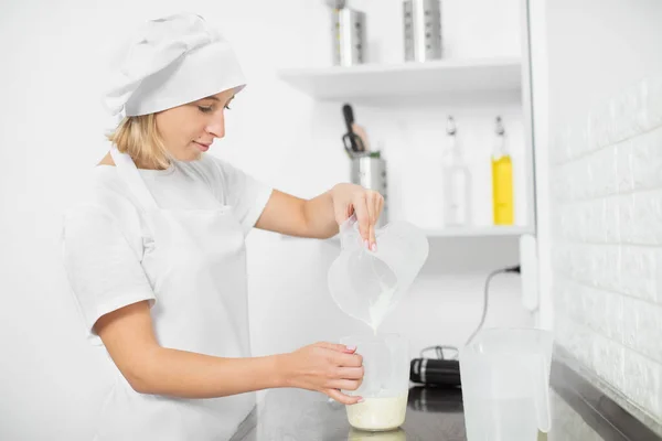 Cottura, cottura e concetto di persone. Giovane donna, pasticciera professionista, che lavora in cucina, prepara la salsa o la ganache per i dolci, versa la panna da una tazza all'altra — Foto Stock