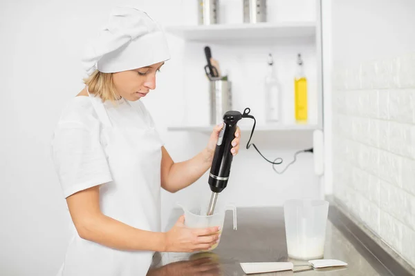 年轻的女性，专业的烘焙师，手里拿着一个潜水器，在测量杯子的重量时，混合着奶油软糖的配料。在糕点店工作，做甜点 — 图库照片