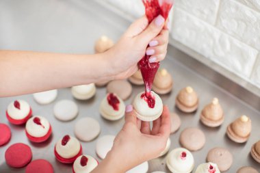 Profesyonel pasta şefinin kadın ellerine yakından bakın, şekerleme poşeti ve tereyağlı beyaz makarna ve sıkılmış kırmızı meyve reçeli. Arka planda makaron satırları