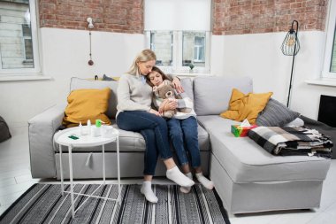 Grip, koronavirüs ve soğuk konsept. Endişeli, sarışın, 40 yaşında bir anne, hasta, genç kızına sarılıyor ve ateşini ölçüyor.