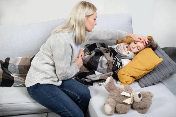 Concepto de gripe, resfriado y fiebre. Cuidadosa madre de mediana edad cariñosa y confiada tocando la frente de su triste hija enferma, acostada en la cama con fiebre y termómetro en la boca —  Fotos de Stock