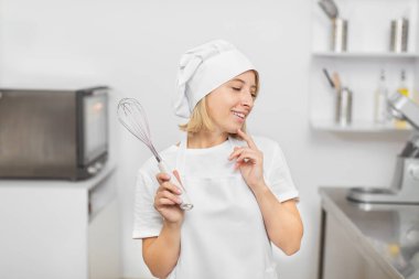 Şekerleme atölyesi. Genç, güzel, sarışın bir kadının portresi, profesyonel pasta şefi, modern mutfağın içinde çırpılmış çırpılmış olarak duruyor ve inanılmaz çalışmalarını hayal ediyor.