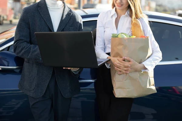 Gros plan recadré vue de face de personnes occupées modernes, homme et femme, travaillant sur ordinateur portable PC, tout en s'appuyant sur la voiture moderne au parking public près du centre commercial après les achats — Photo