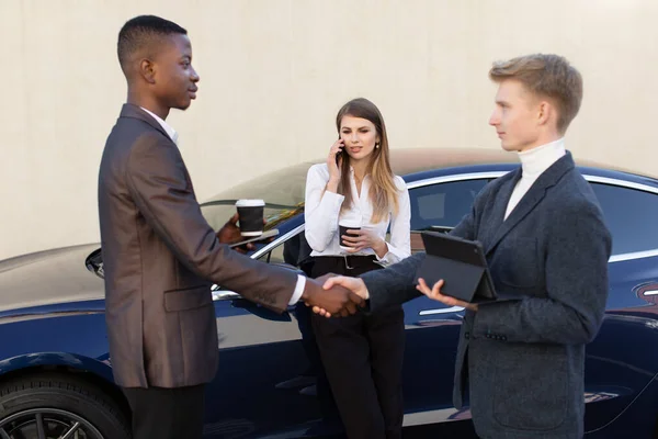 Pause café sur la route, concept d'affaires et d'accord. Jeunes trois collègues multiraciaux d'affaires debout à l'extérieur près de la nouvelle voiture. Hommes poignée de main, téléphone femme parlant — Photo