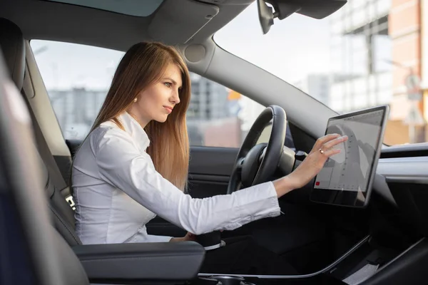 Concept de voiture électrique intelligente. Jolie femme en tenue formelle, contrôlant la voiture autonome électrique moderne avec un écran de tableau de bord numérique, commutant le mode pilote automatique — Photo